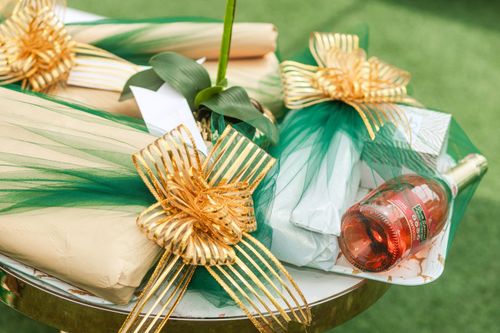 Free A close-up of beautifully wrapped gifts with green and gold decorations and a bottle of rose wine. Stock Photo