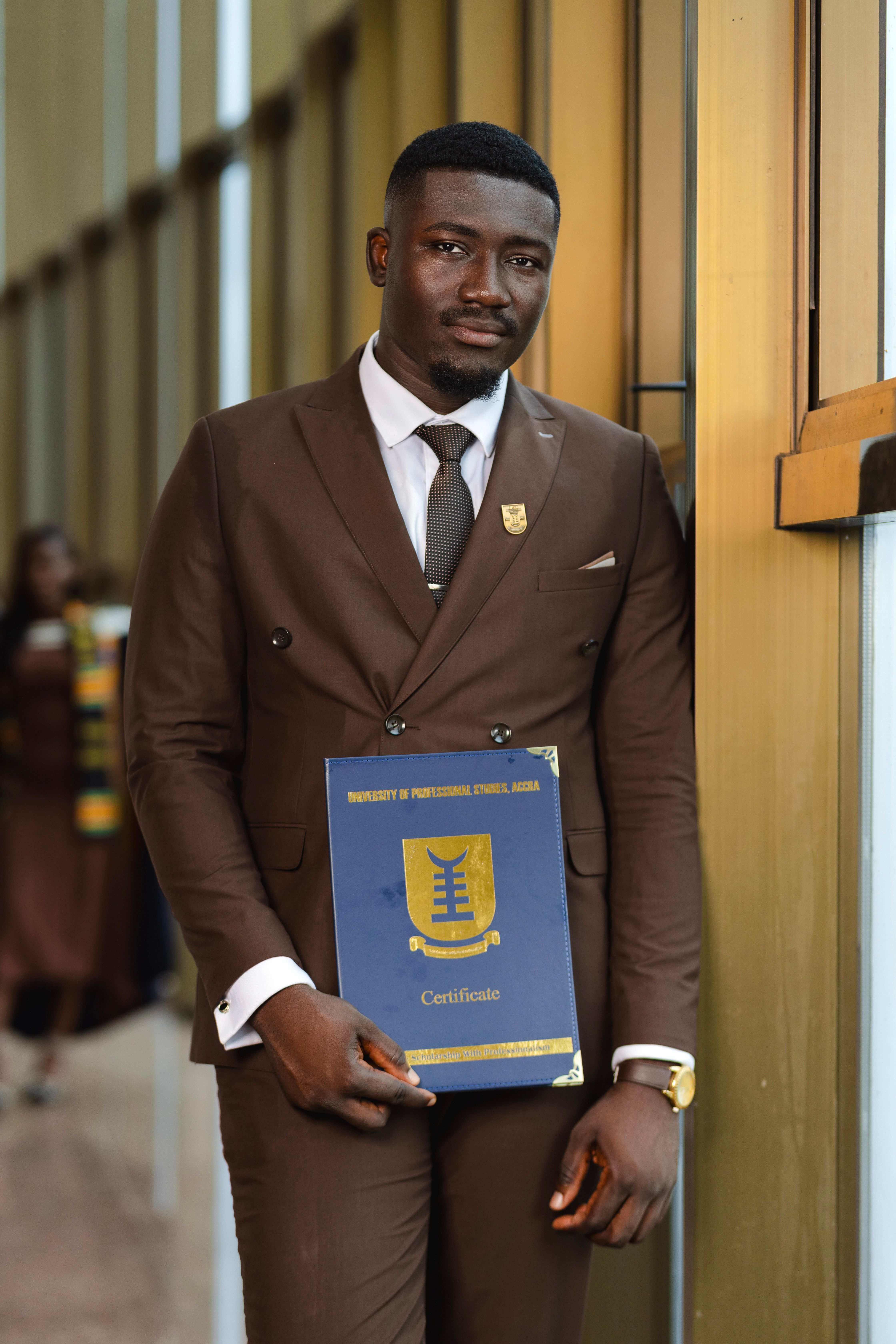 Young adult male in formal attire holding a university certificate at a graduation ceremony.