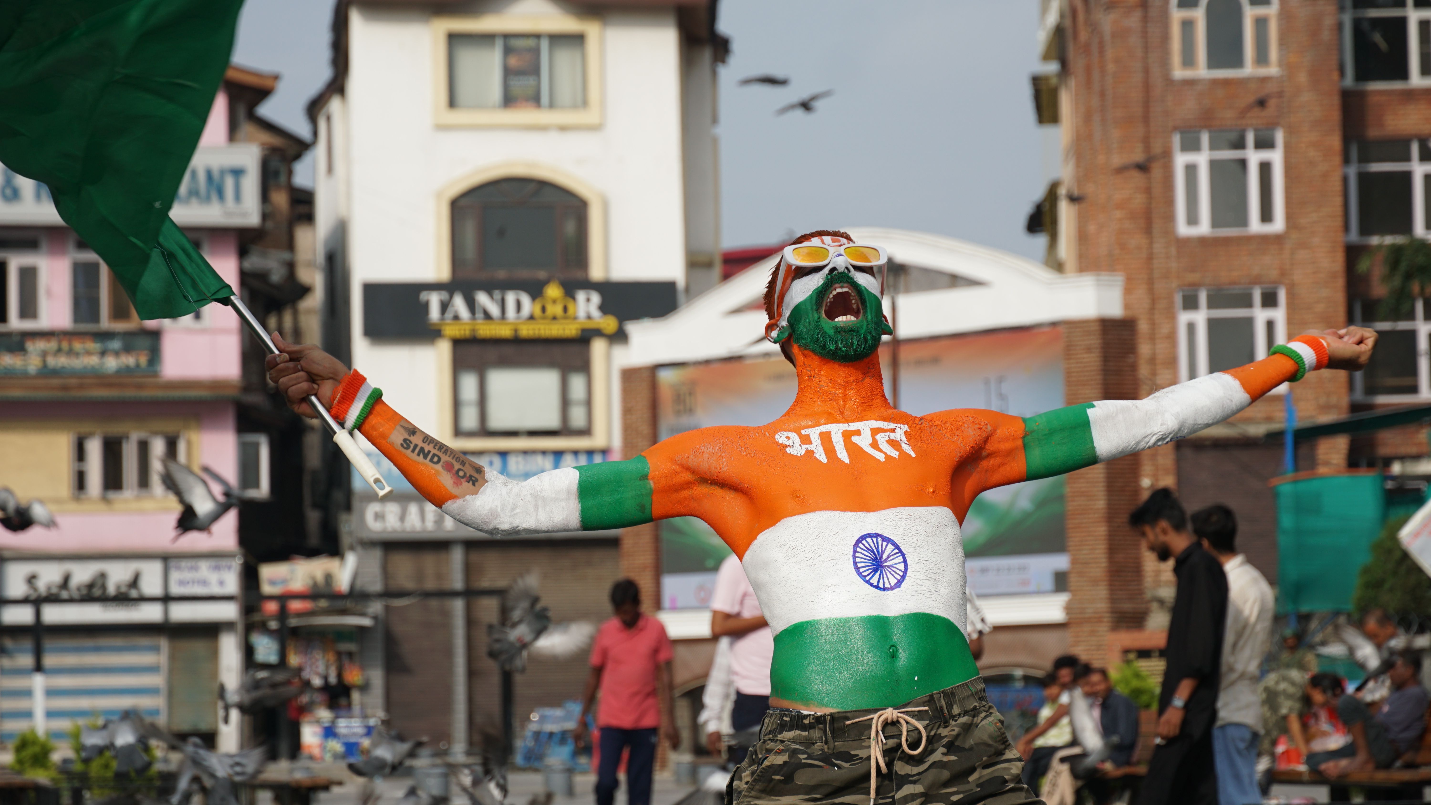 A man passionately celebrates with Indian flag body paint and waving flag outdoors.