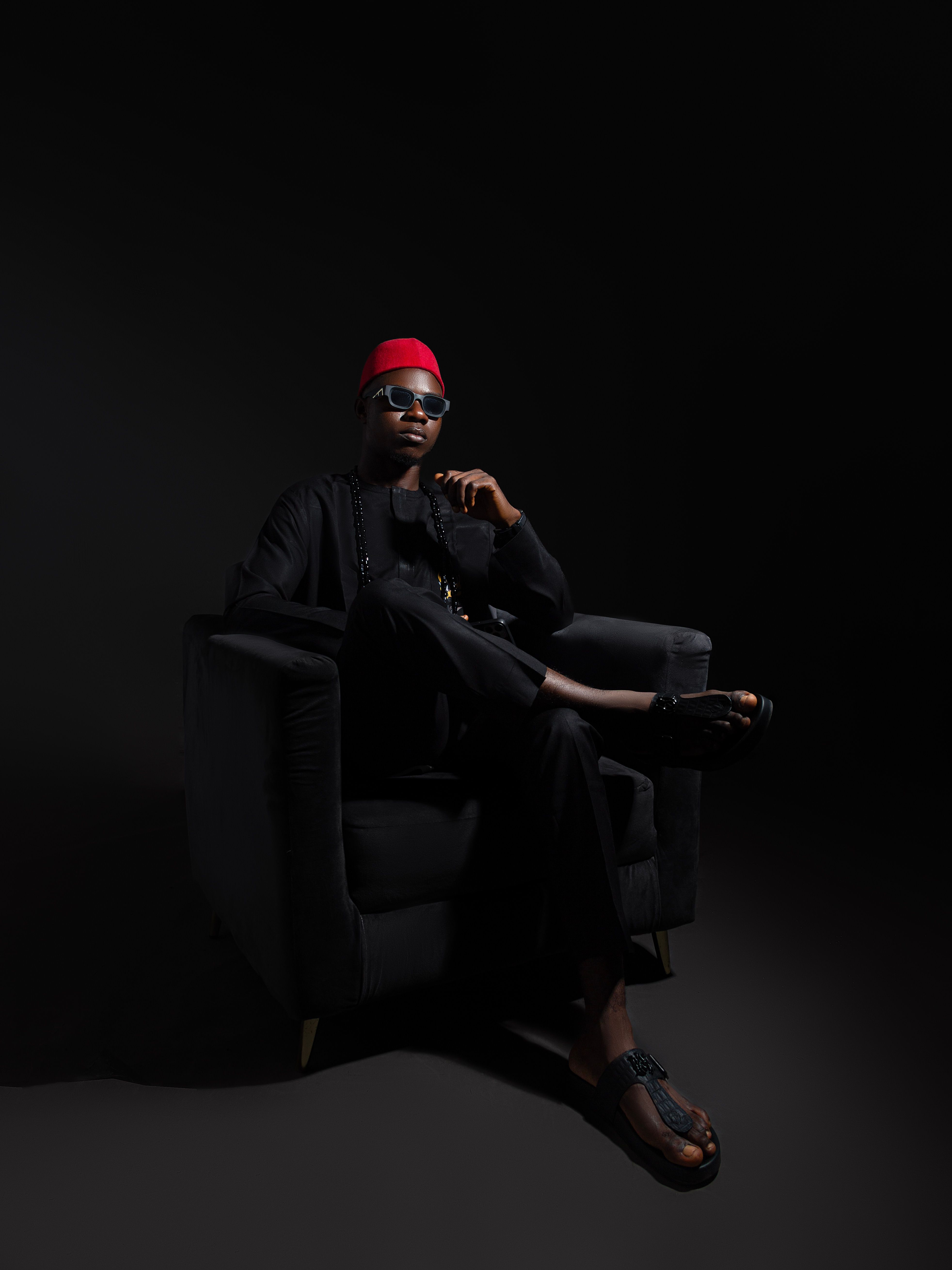 Elegant man in traditional clothing seated on a chair against a dark background.