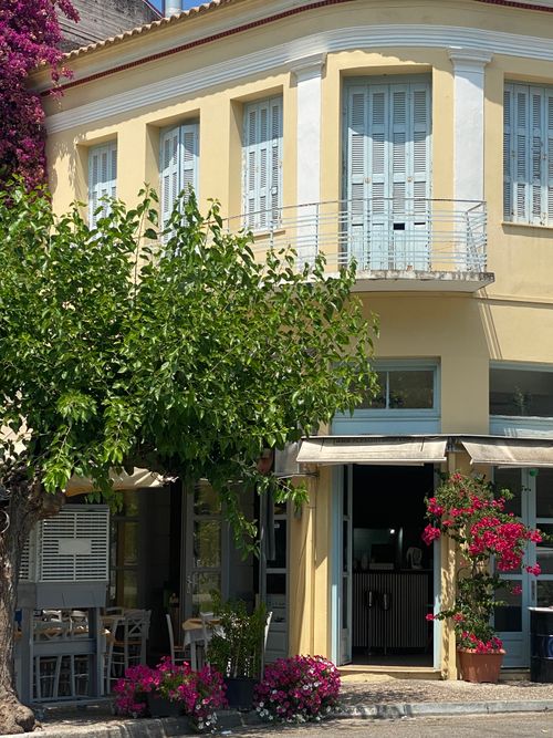Free A quaint cafe in Greece, adorned with vibrant flowers and bathed in summer sunlight. Stock Photo