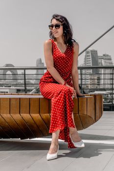 A fashionable woman in a red polka dot dress poses outdoors with a city skyline in Baku.