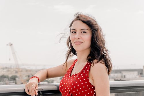 Free A woman in a red polka dot dress smiles outdoors in Baku with cityscape in the background. Stock Photo