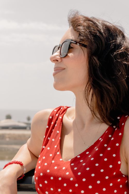Free Smiling woman wearing sunglasses and red polka dot dress, enjoying a sunny day outdoors. Stock Photo