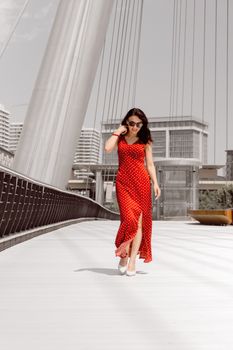 Woman in red dress walking across modern bridge in Baku, Azerbaijan.
