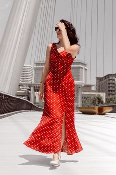 Chic woman in red polka dot dress walks on a modern bridge in Baku.