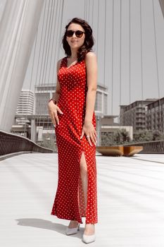 Stylish woman in a red polka dot dress poses elegantly on a modern bridge in Baku, Azerbaijan.