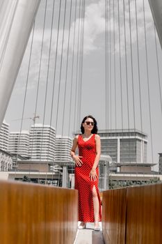Elegant woman in red dress poses confidently on modern bridge in Baku, Azerbaijan.