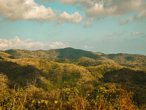 Free Beautiful mountain range with lush greenery under a vibrant blue sky and fluffy clouds. Stock Photo