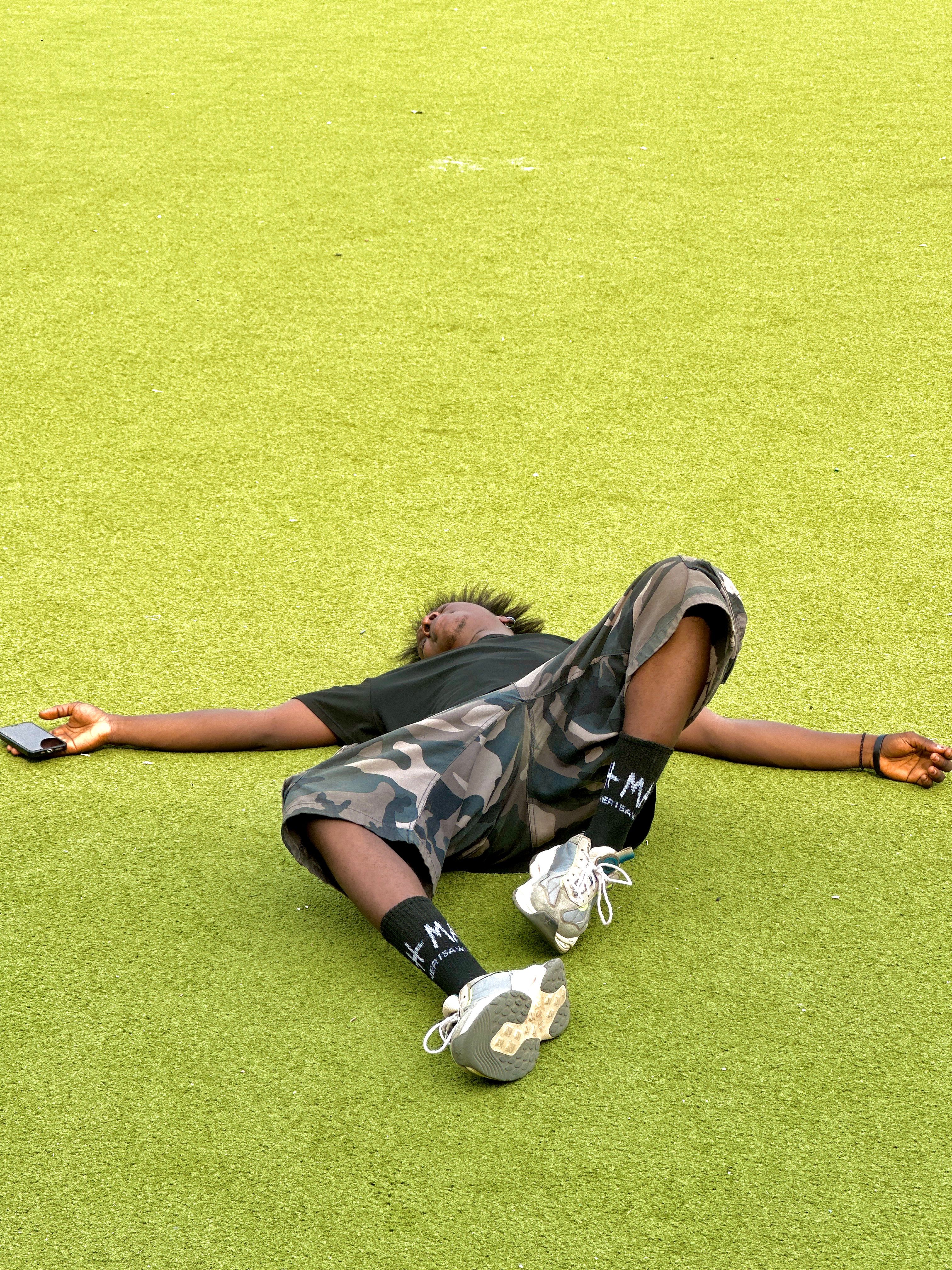 A relaxed person in camo shorts lies on vibrant green grass outdoors, enjoying leisure time.