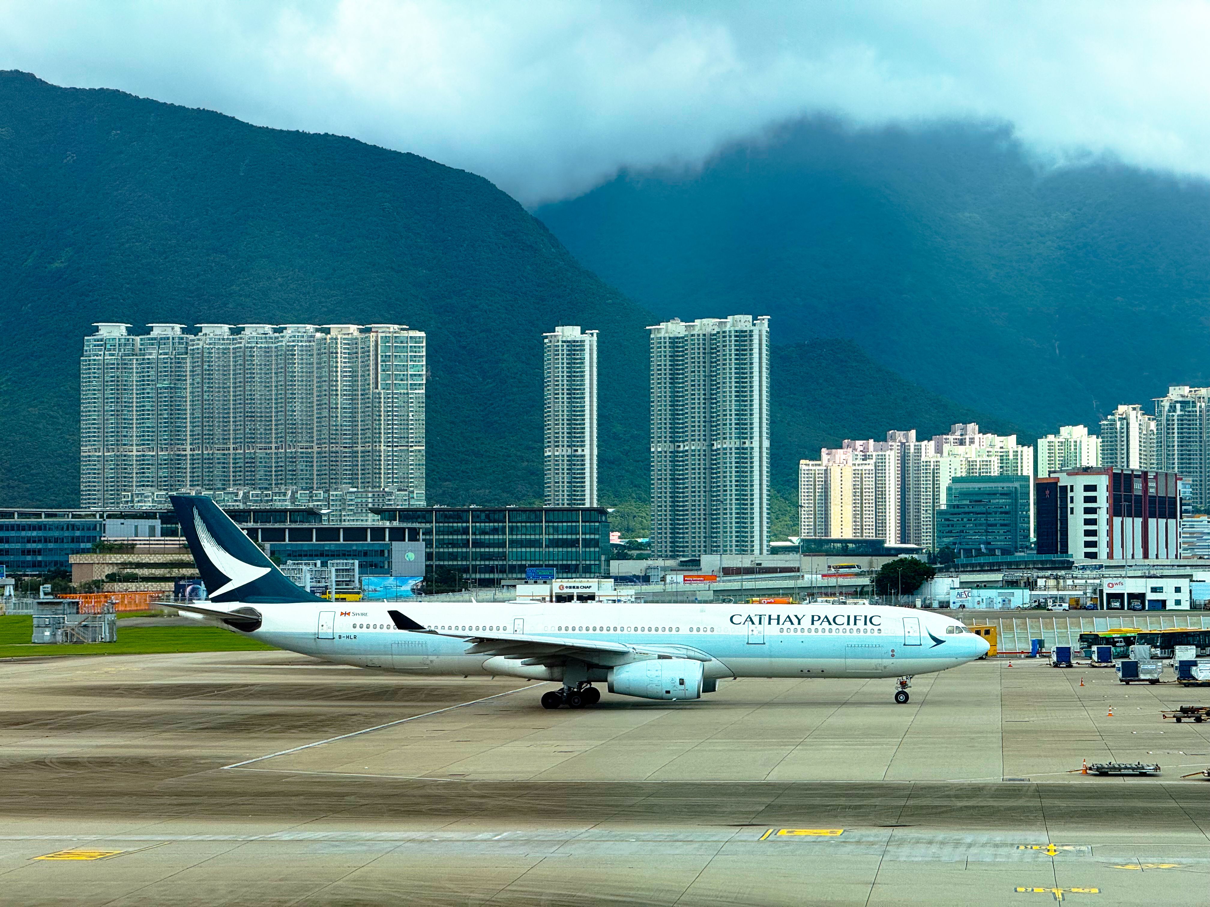 Cathay Pacific airplane taxiing on runway with Hong Kong skyline and mountains in the background. — arriving in Hong Kong