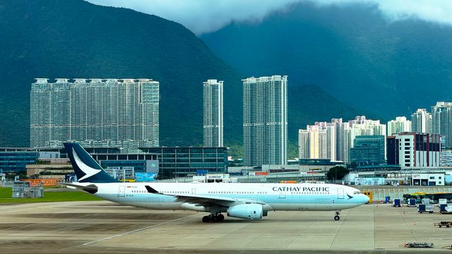 Cathay Pacific airplane taxiing on runway with Hong Kong skyline and mountains in the background. — lounges at Hong Kong Airport