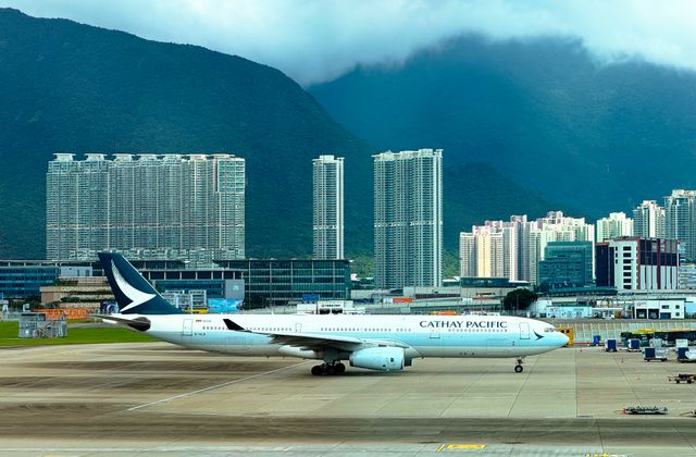 Cathay Pacific airplane taxiing on runway with Hong Kong skyline and mountains in the background. — arriving in Hong Kong