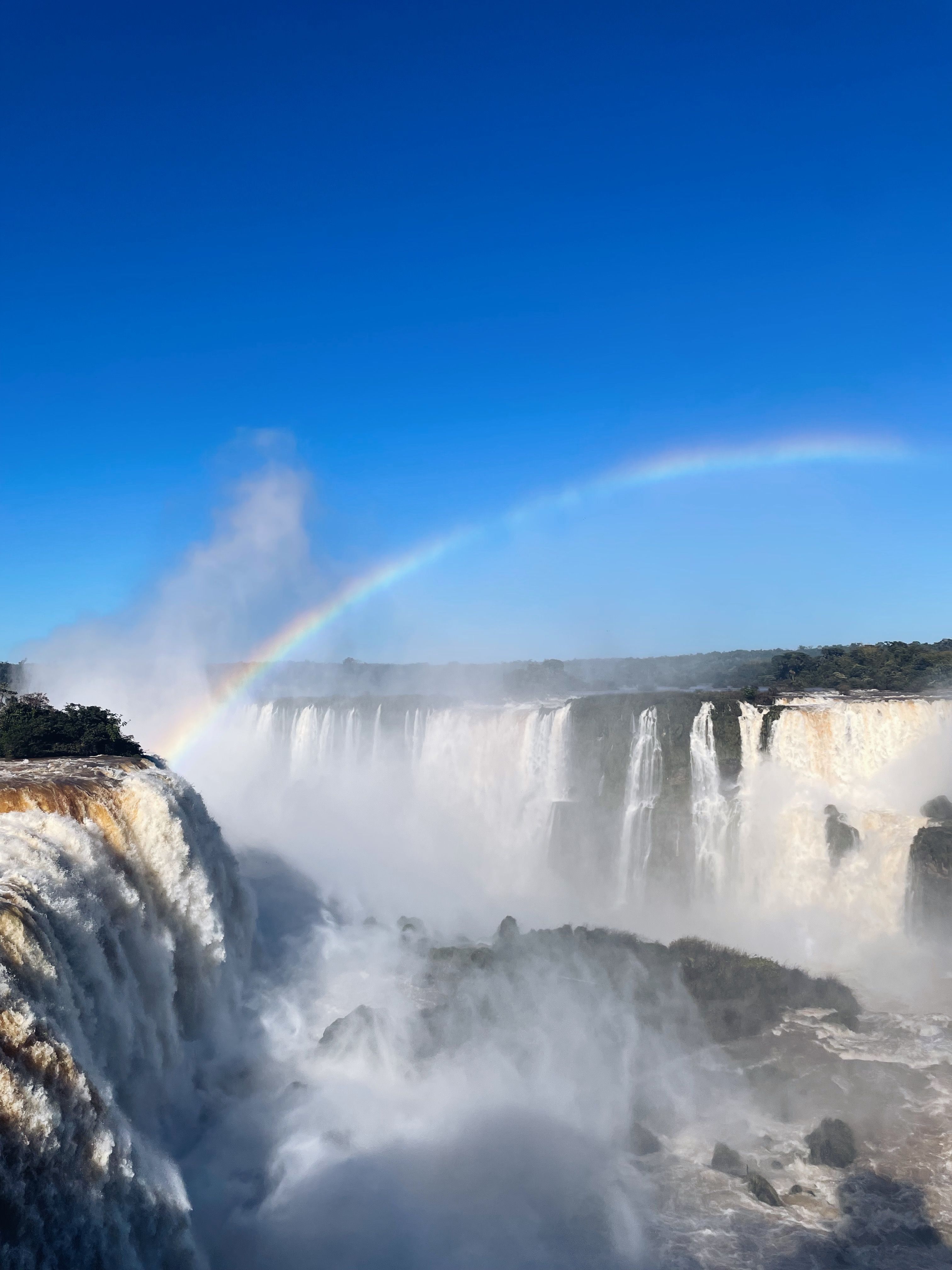 Majestic view of Iguazu Falls with a beautiful rainbow under clear blue sky.
