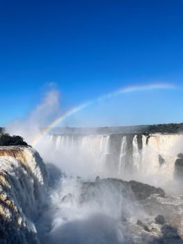 Majestic view of Iguazu Falls with a beautiful rainbow under clear blue sky.