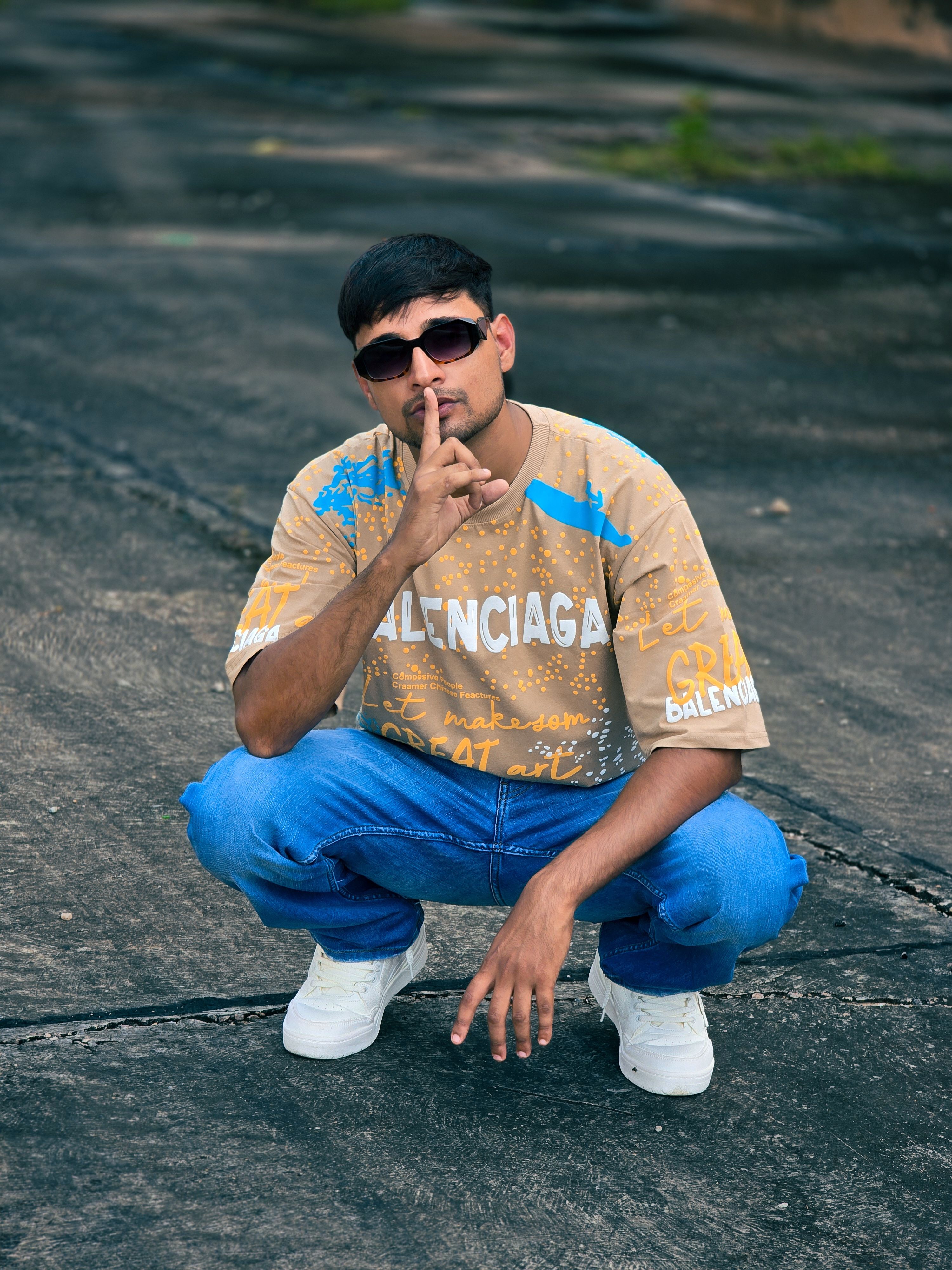 Young man in casual attire posing outdoors with finger on lips, expressing silence.