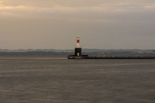 Free Peaceful view of a lighthouse on a breakwater during a calm evening at sea. Stock Photo