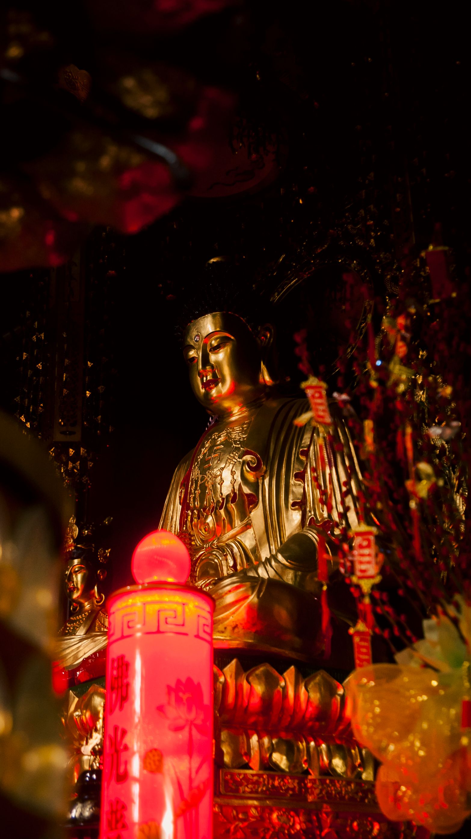 Illuminated golden Buddha statue surrounded by red lanterns creates a spiritual ambiance.