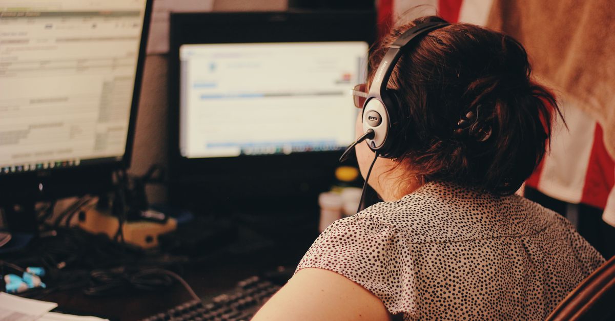 Mujer utilizando dos monitores y auriculares en un entorno de centro de llamadas.