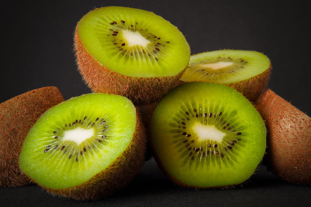 Sliced kiwi fruit showing bright green flesh and black seeds on white background