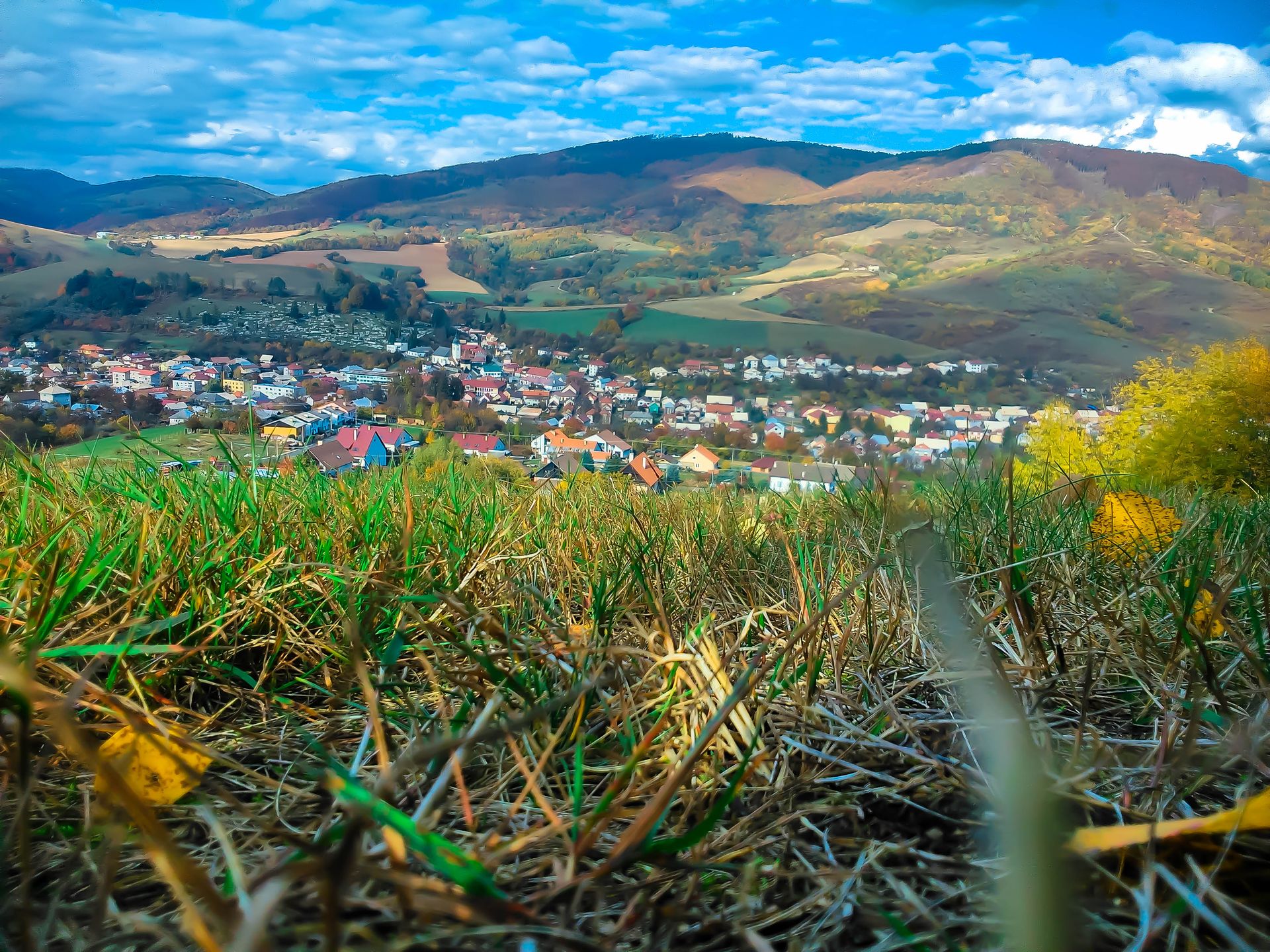 Serene view of a quaint village nestled within lush rolling hills and vibrant grass, bathed in daylight.