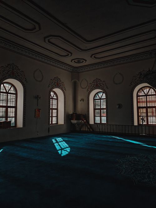 Free Beautiful mosque interior with patterned carpets and arched windows casting shadows. Stock Photo