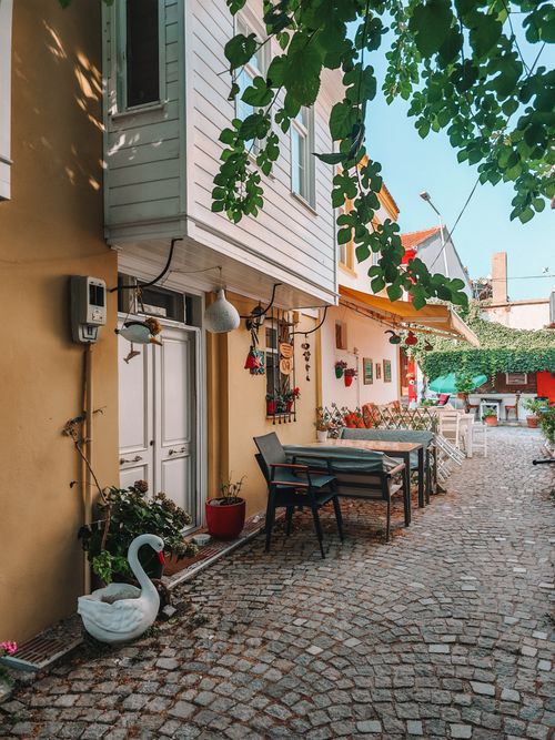 Free Serene cobblestone street with vibrant facades, outdoor seating, and lush greenery. Ideal for lifestyle and travel themes. Stock Photo