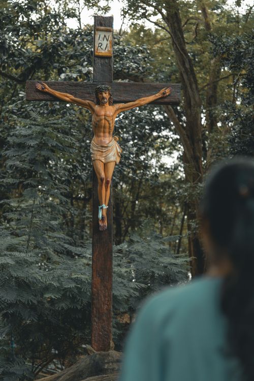 Free A wooden crucifix with Jesus statue in a forested area, viewed by a person Stock Photo