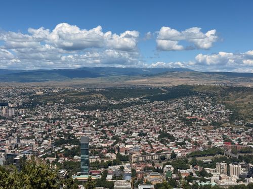 Free Aerial view of Tbilisi, Georgia, showcasing cityscape against mountain backdrop under a blue sky. Stock Photo