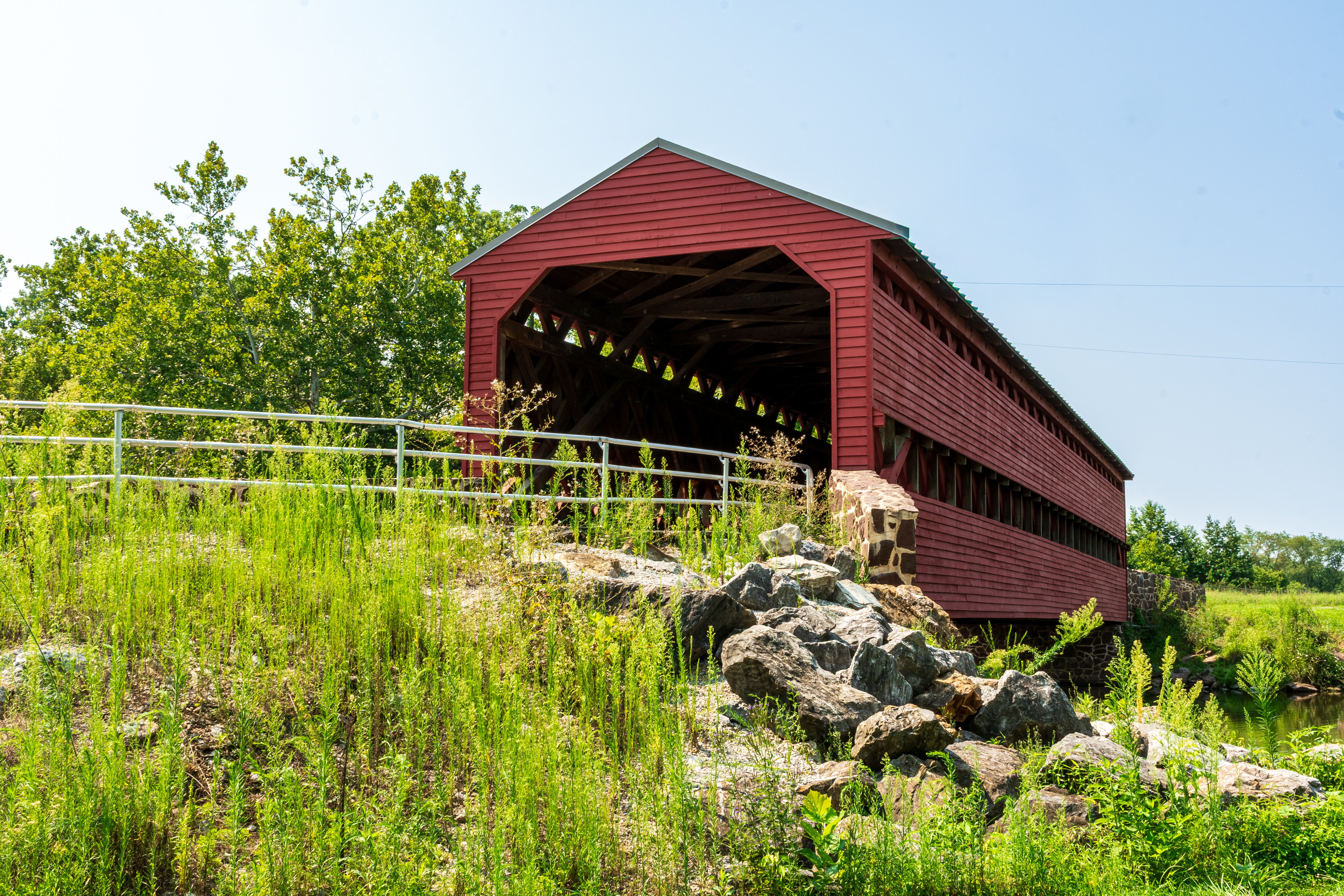 Idyllic red covered bridge surrounded by lush greenery on a sunny summer day.