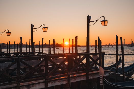 Stunning sunset view over the Venice lagoon with silhouetted gondolas and wooden piers.