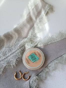 A stylish flat lay of lace lingerie, Lamel face powder, and hoop earrings.