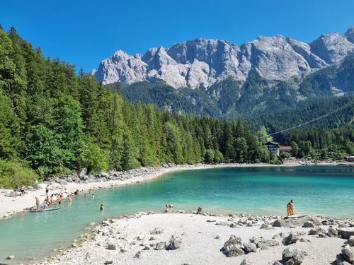 Free A vibrant alpine lake with people enjoying a sunny day, surrounded by mountains. Stock Photo