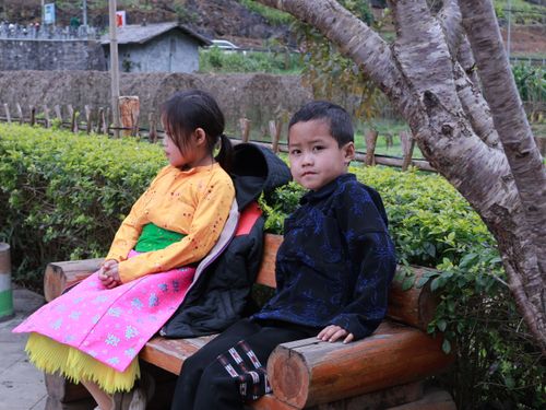 Free Two children in colorful traditional clothes sit on a wooden bench outdoors. Stock Photo