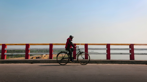 Free A man cycling across a vibrant painted bridge with scenic urban and river views in Khulna, Bangladesh. Stock Photo