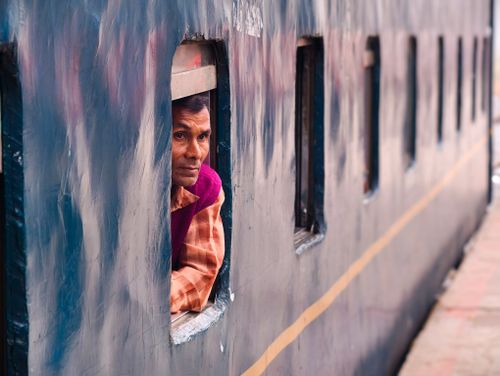 Free A man in Bangladesh peers thoughtfully out of a train window as it travels, capturing a moment of transit. Stock Photo