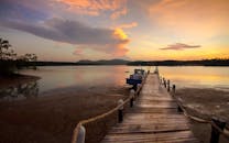 平静的湖面上映着美丽的日落，木码头和远处的山脉构成宁静的度假景致