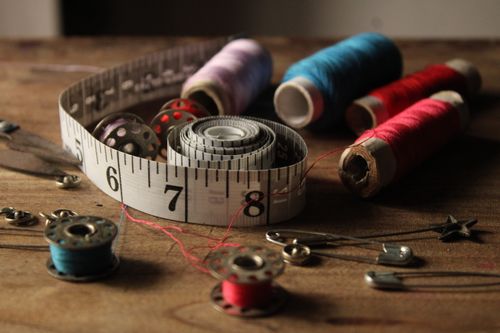 Free A collection of vibrant sewing materials including threads, bobbins, and a measuring tape on a wooden background. Stock Photo