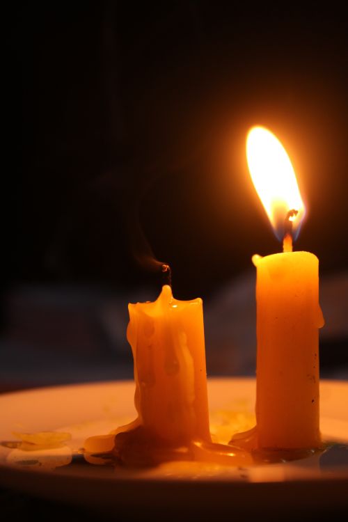 Free Two candles with melting wax, one extinguished, against a dark background, creating a warm glow. Stock Photo