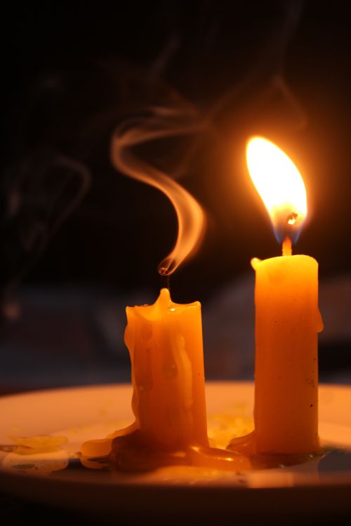 Free Close-up of a glowing candle with smoke gently rising from the extinguished one beside it. Stock Photo
