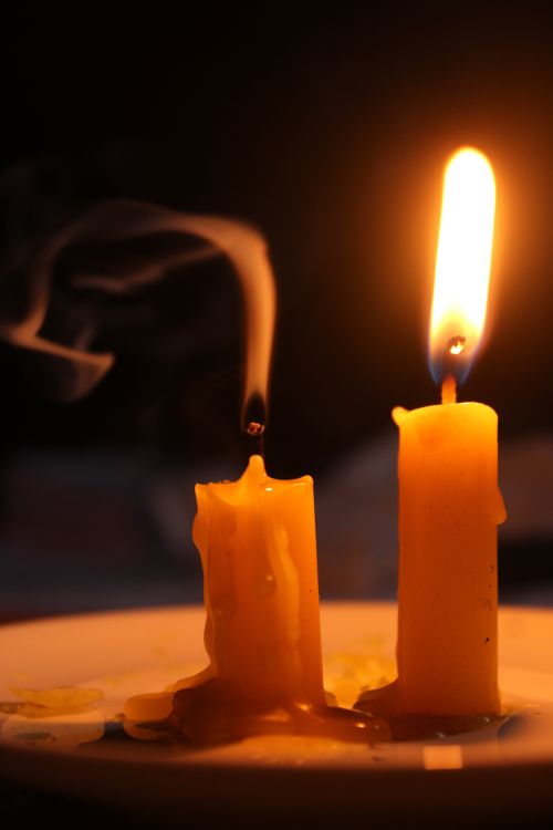 Free Intimate close-up of two candles, one lit and one extinguished, with soft wax drips and ambient light. Stock Photo