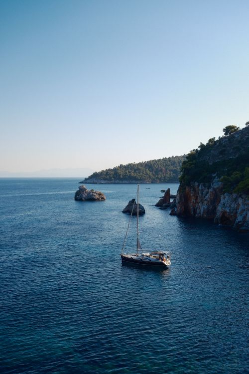 Free Scenic view of a sailboat near a rocky coastline with clear blue waters under a sunny sky. Stock Photo