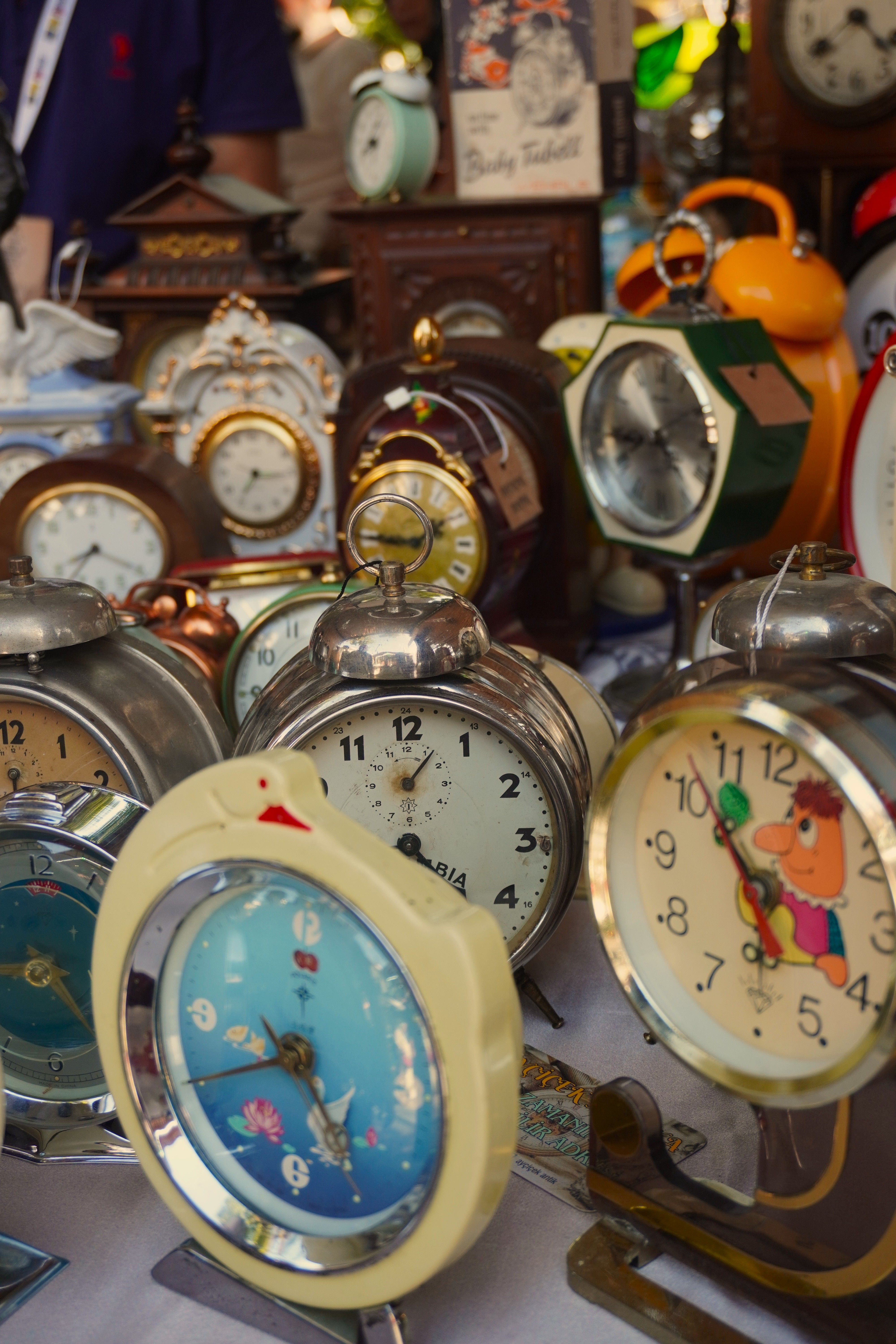 A variety of vintage alarm clocks on display at an outdoor flea market under natural light.