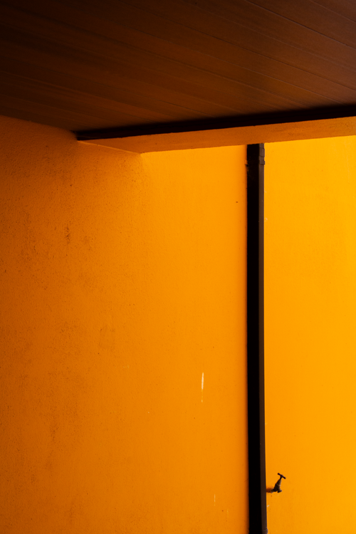 Free A vibrant yellow wall with a black vertical pipe under a dark ceiling corner. Stock Photo