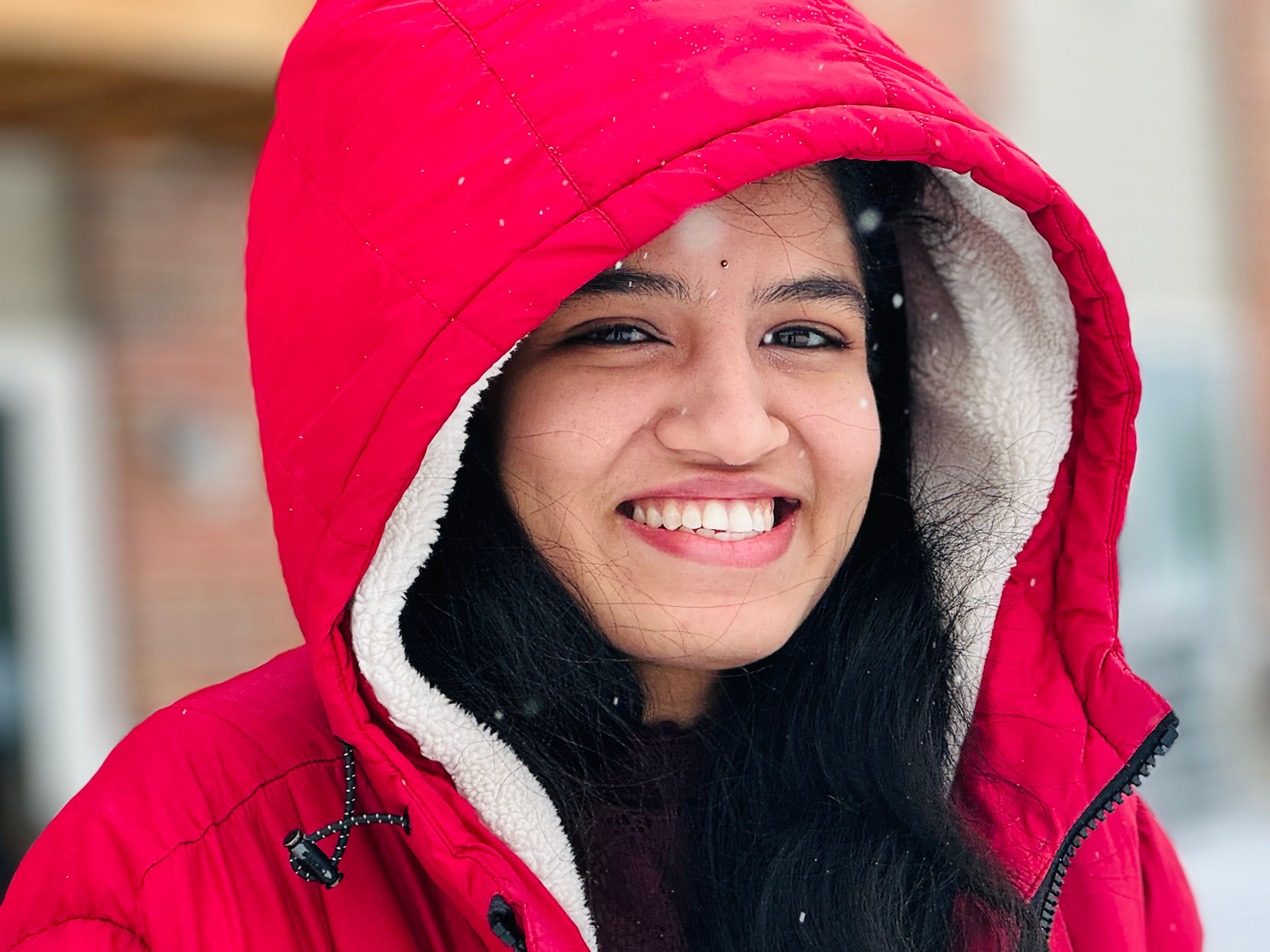 Young woman smiling outdoors in a red winter jacket with snowflakes.
