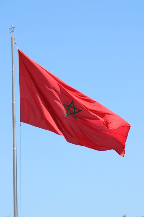 Free The national flag of Morocco features a green star on red, waving against a clear blue sky. Stock Photo