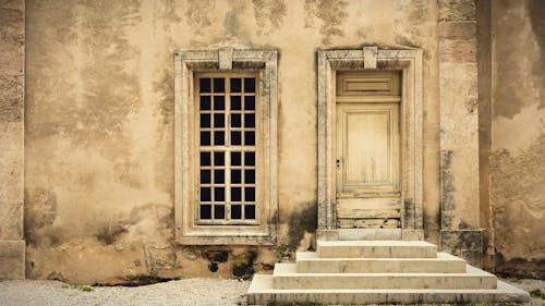 Shabby stone wall of aged house with window and door with steps on street of old city