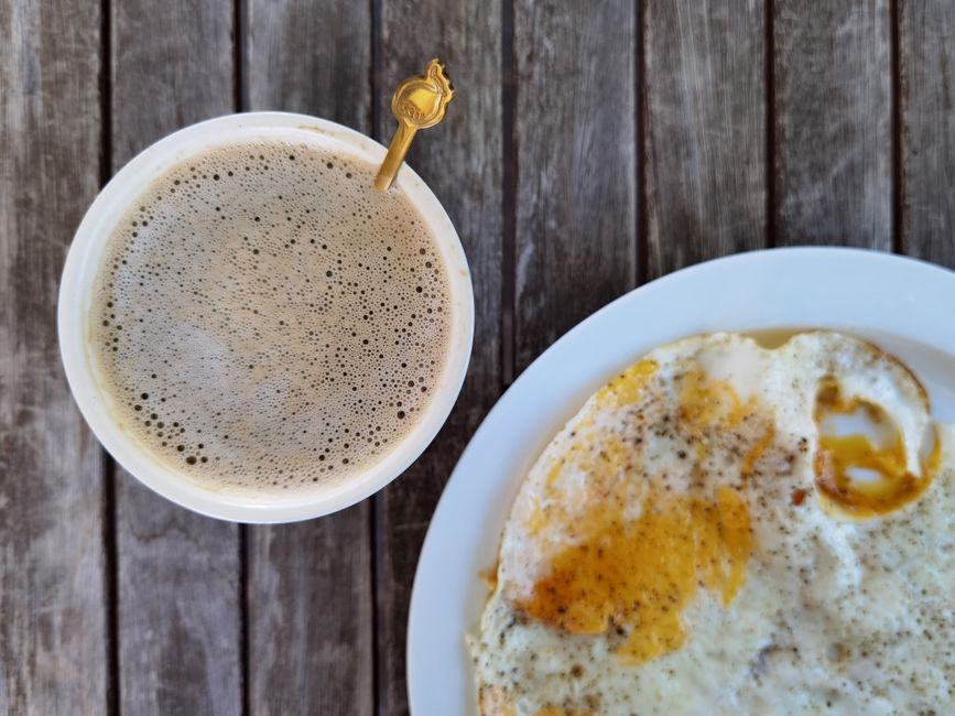 A top-down view of a cup of coffee and a plate of fried eggs on a rustic wood table.