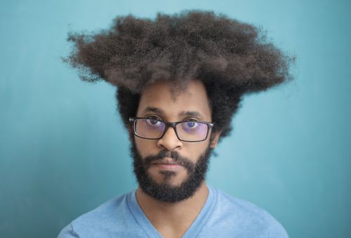 Free Close-up portrait of a man with an afro hairstyle and eyeglasses against a blue background. Stock Photo