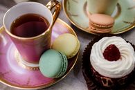 A stylish arrangement of tea, macarons, and a raspberry-topped dessert on ornate dishes.